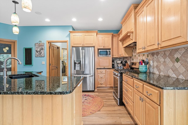 kitchen featuring appliances with stainless steel finishes, light brown cabinetry, dark stone counters, sink, and hanging light fixtures