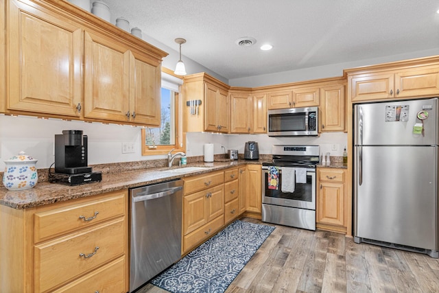 kitchen with light stone countertops, sink, hanging light fixtures, light hardwood / wood-style flooring, and appliances with stainless steel finishes