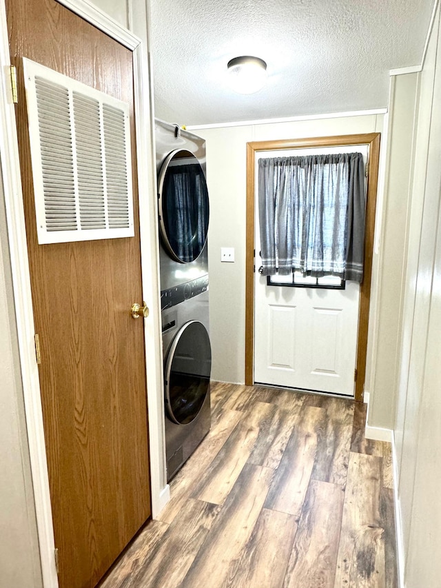 laundry area with ornamental molding, a textured ceiling, stacked washer / dryer, and wood-type flooring