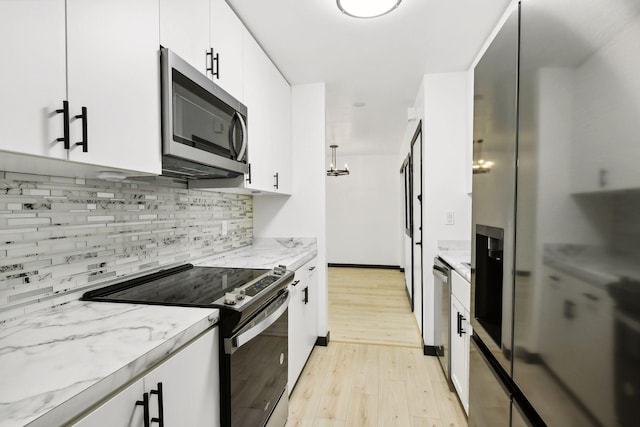 kitchen featuring tasteful backsplash, hanging light fixtures, stainless steel appliances, white cabinets, and light hardwood / wood-style flooring