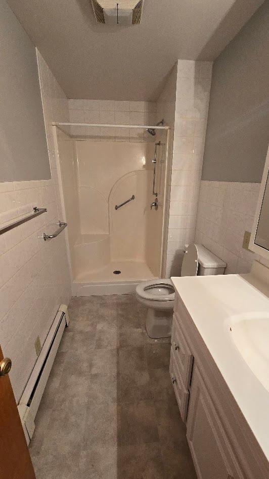 bathroom featuring tile walls, vanity, toilet, and walk in shower