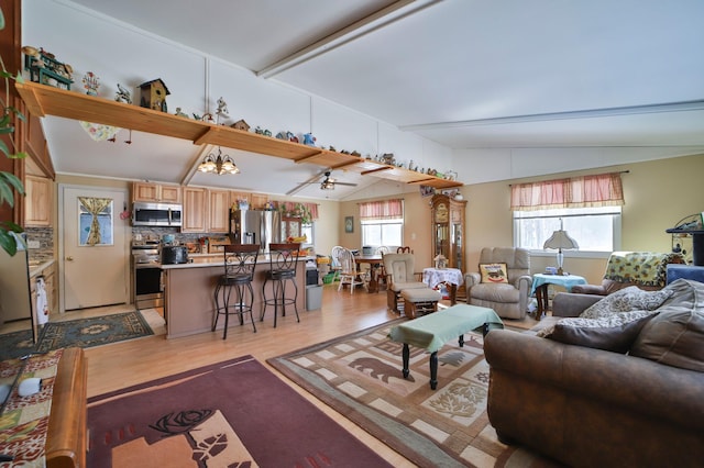 living area with a notable chandelier, vaulted ceiling, and light wood finished floors