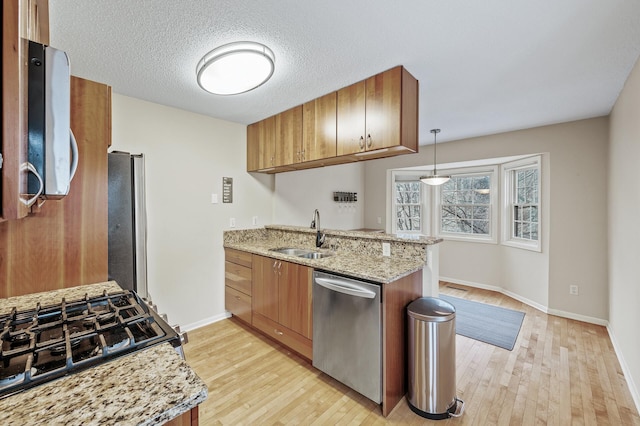 kitchen with sink, hanging light fixtures, appliances with stainless steel finishes, light stone countertops, and light hardwood / wood-style floors