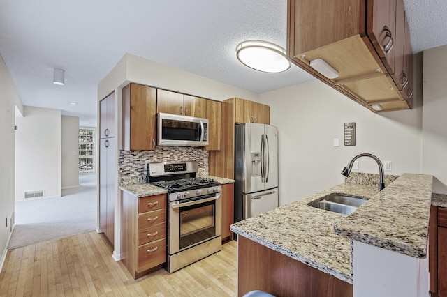 kitchen with sink, light stone counters, light hardwood / wood-style flooring, stainless steel appliances, and backsplash