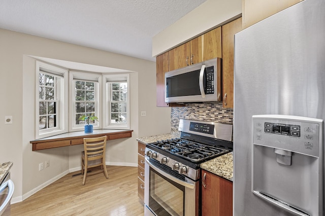 kitchen featuring light stone counters, a textured ceiling, light hardwood / wood-style flooring, appliances with stainless steel finishes, and decorative backsplash