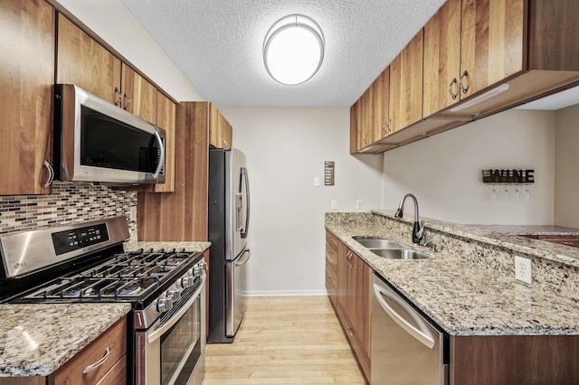 kitchen featuring light stone counters, appliances with stainless steel finishes, sink, and light hardwood / wood-style flooring