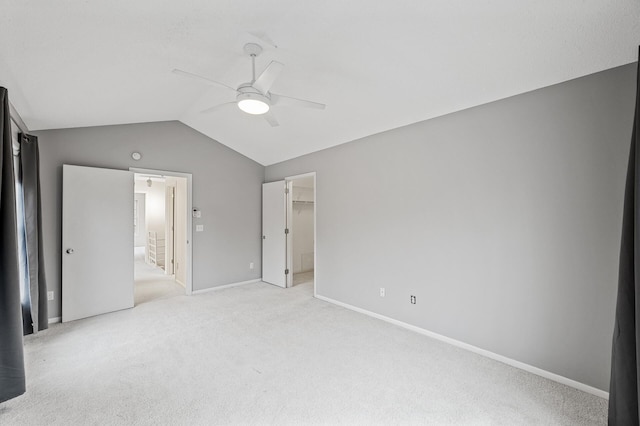 unfurnished bedroom featuring vaulted ceiling, a walk in closet, light colored carpet, and ceiling fan