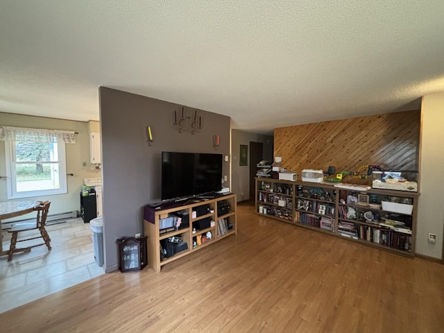 living room with light hardwood / wood-style floors, wood walls, a textured ceiling, and a baseboard radiator