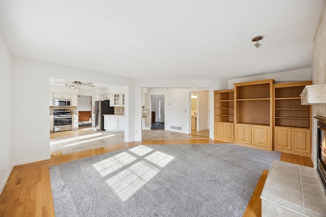 unfurnished living room featuring a fireplace, light hardwood / wood-style floors, and ceiling fan