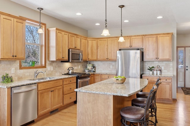 kitchen featuring stainless steel appliances, a kitchen island, a sink, and light wood-style floors