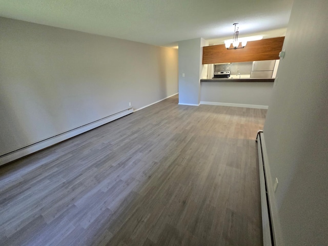 unfurnished living room featuring baseboard heating, a chandelier, and hardwood / wood-style floors