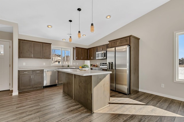 kitchen with a center island, stainless steel appliances, lofted ceiling, decorative light fixtures, and light hardwood / wood-style flooring