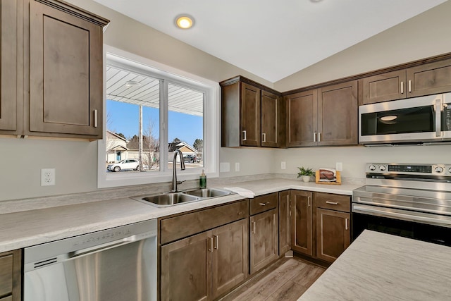 kitchen with dark brown cabinets, sink, vaulted ceiling, appliances with stainless steel finishes, and light hardwood / wood-style floors