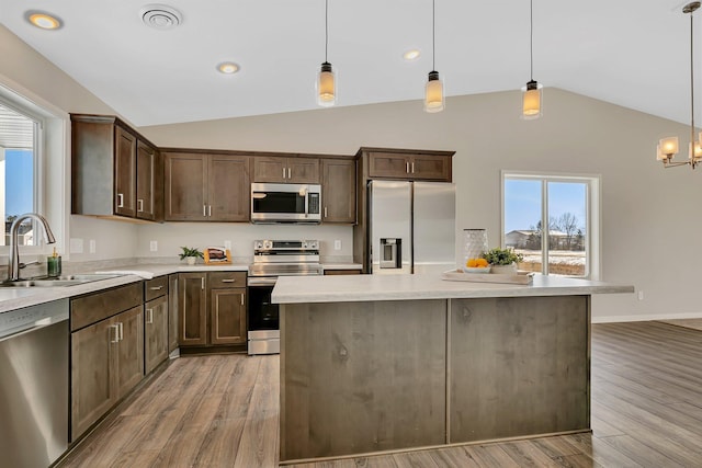 kitchen with lofted ceiling, sink, appliances with stainless steel finishes, and hanging light fixtures