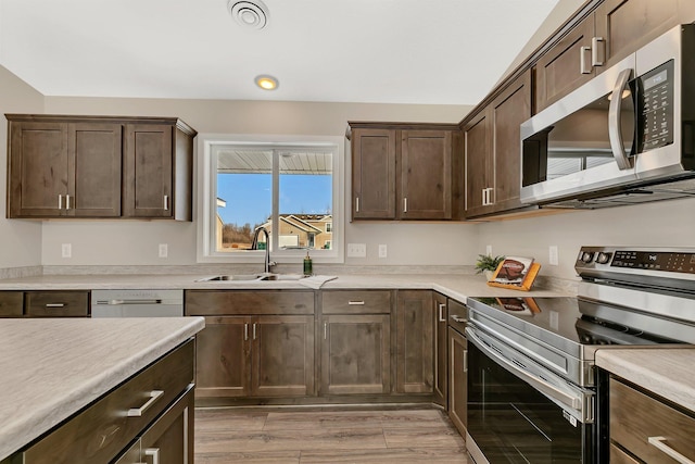 kitchen with dark brown cabinetry, appliances with stainless steel finishes, sink, and light wood-type flooring