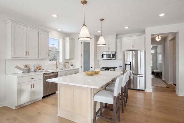 kitchen with a kitchen island, appliances with stainless steel finishes, decorative light fixtures, light hardwood / wood-style floors, and white cabinetry