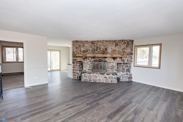 unfurnished living room with a healthy amount of sunlight, a baseboard radiator, dark hardwood / wood-style floors, and a stone fireplace