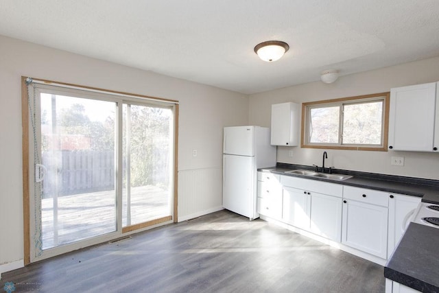 kitchen with white cabinets, a sink, dark countertops, freestanding refrigerator, and wood finished floors