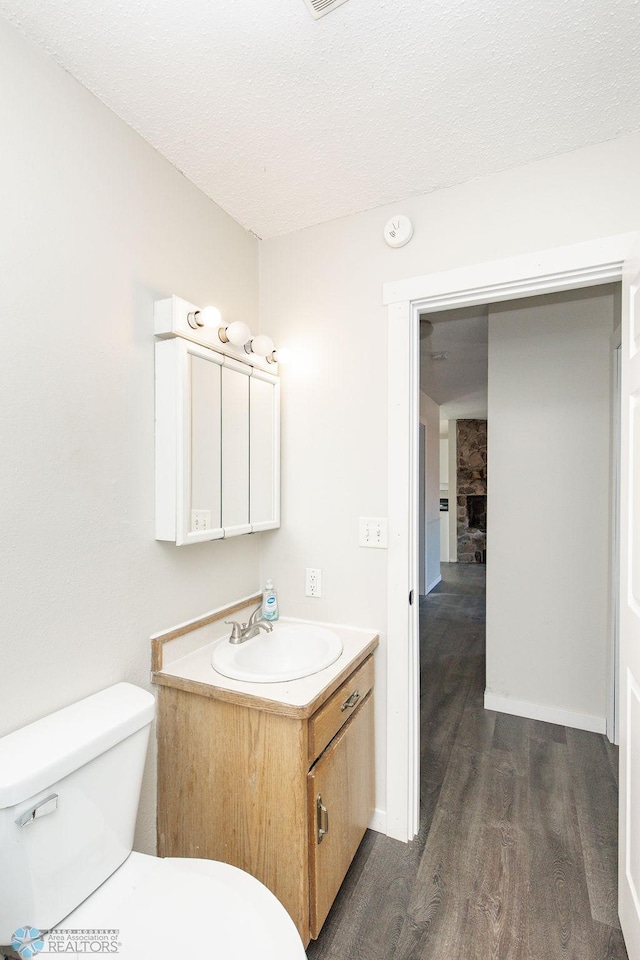 half bath featuring wood finished floors, a textured ceiling, vanity, toilet, and visible vents