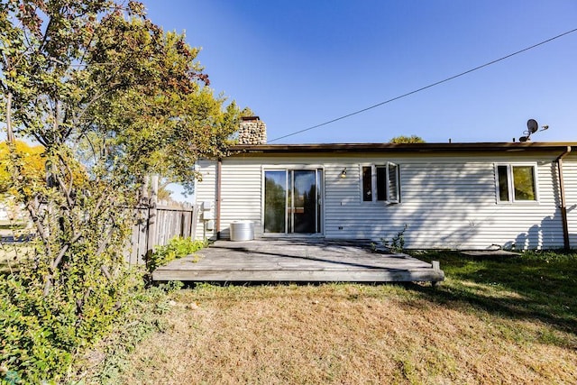 back of property with a lawn, a chimney, fence, and a deck
