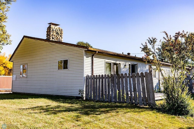 view of side of property with a lawn, a chimney, and fence