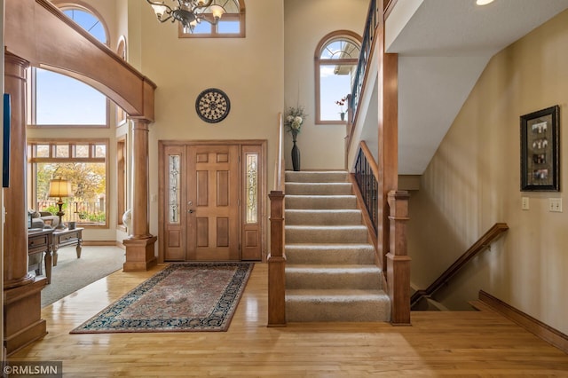 foyer entrance featuring a chandelier, decorative columns, hardwood / wood-style flooring, and high vaulted ceiling