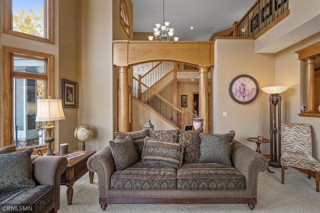 carpeted living room featuring a high ceiling, ornate columns, and an inviting chandelier