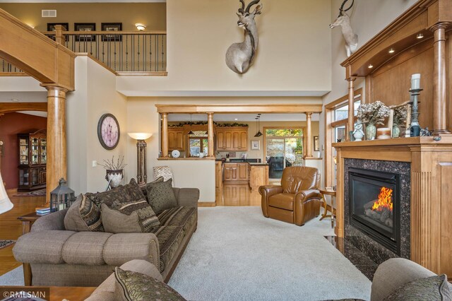 living room with a premium fireplace, decorative columns, light carpet, and a towering ceiling