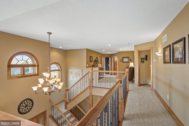 hallway with light carpet, a textured ceiling, and an inviting chandelier