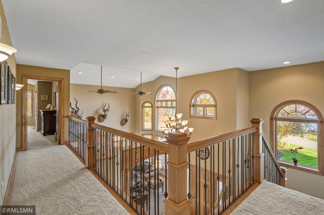 corridor with a healthy amount of sunlight, a textured ceiling, and light colored carpet