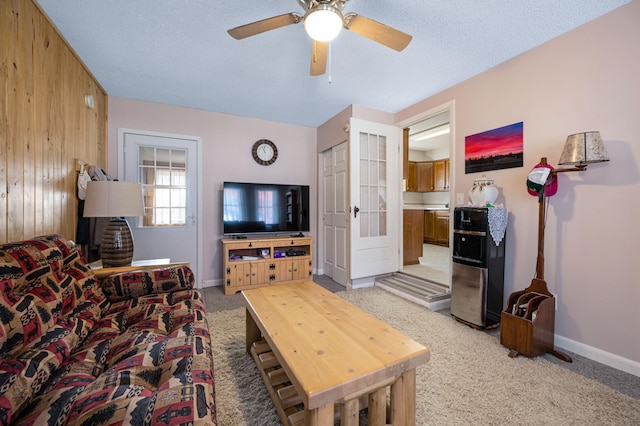 carpeted living room featuring wood walls, a textured ceiling, and ceiling fan