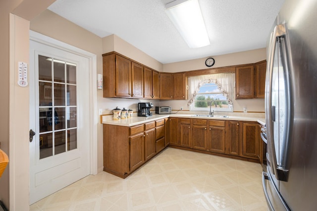 kitchen with sink, a textured ceiling, and stainless steel refrigerator