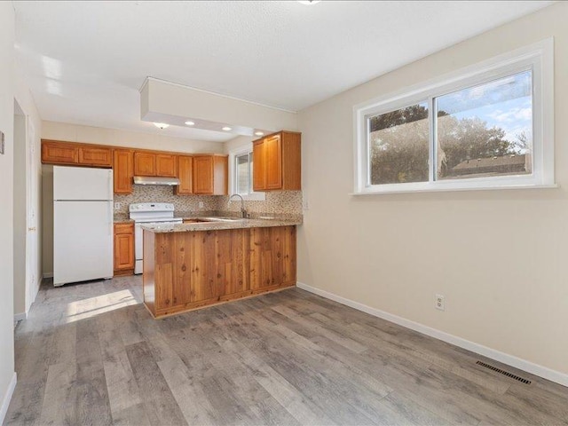 kitchen featuring white appliances, sink, decorative backsplash, light hardwood / wood-style floors, and kitchen peninsula