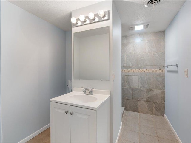 bathroom with tile patterned floors, vanity, a textured ceiling, and tiled shower