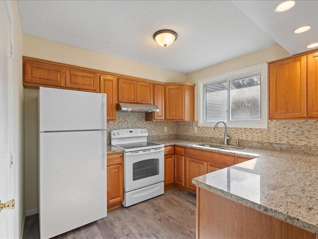 kitchen with white appliances, backsplash, sink, light hardwood / wood-style flooring, and light stone countertops