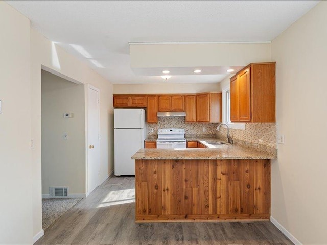 kitchen with white appliances, backsplash, sink, light hardwood / wood-style flooring, and kitchen peninsula