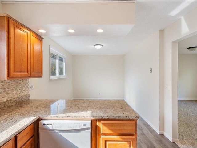 kitchen featuring white dishwasher, light hardwood / wood-style flooring, decorative backsplash, light stone countertops, and kitchen peninsula