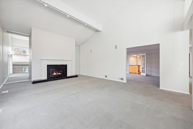 unfurnished living room with light colored carpet, beam ceiling, high vaulted ceiling, and track lighting