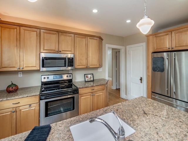 kitchen featuring stainless steel appliances, sink, light stone countertops, decorative light fixtures, and light hardwood / wood-style floors