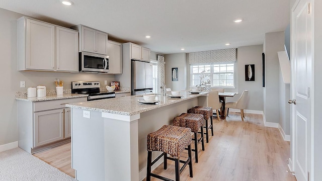 kitchen with appliances with stainless steel finishes, light wood-type flooring, light stone counters, a breakfast bar area, and a kitchen island with sink