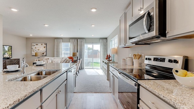 kitchen featuring sink, light wood-type flooring, a textured ceiling, stainless steel appliances, and light stone counters