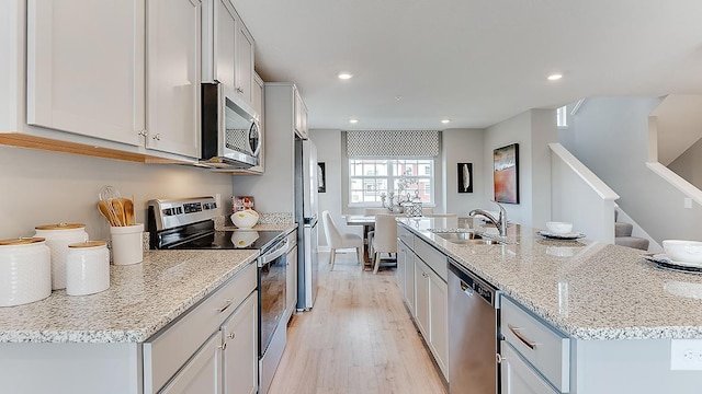 kitchen with an island with sink, appliances with stainless steel finishes, light stone countertops, light hardwood / wood-style flooring, and sink