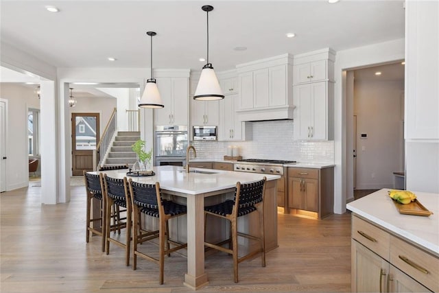 kitchen with hardwood / wood-style floors, white cabinets, an island with sink, stainless steel appliances, and sink