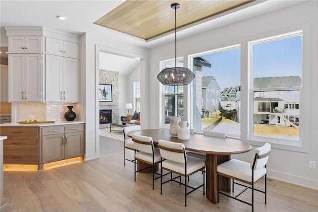 dining area with a stone fireplace, light wood-type flooring, and wood ceiling