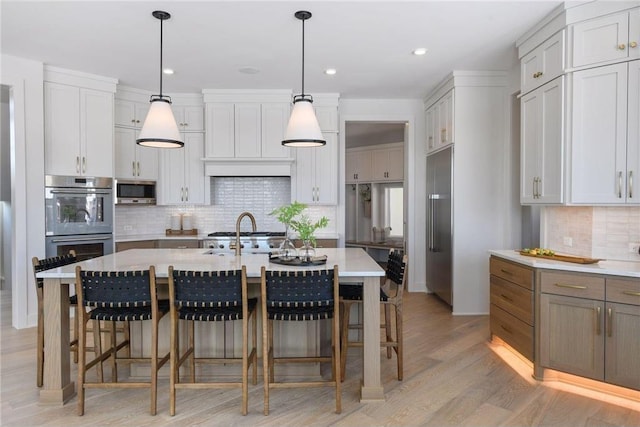 kitchen featuring decorative backsplash, an island with sink, hanging light fixtures, and light hardwood / wood-style floors