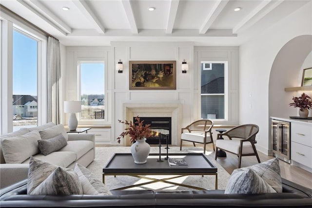 living room featuring wine cooler, a premium fireplace, beam ceiling, and light hardwood / wood-style flooring