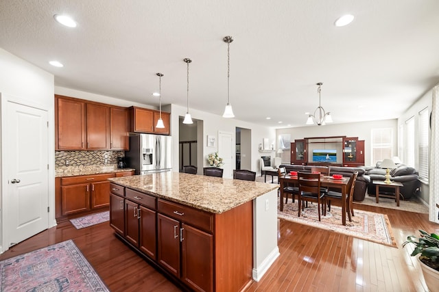 kitchen featuring light stone countertops, stainless steel fridge, backsplash, decorative light fixtures, and a center island