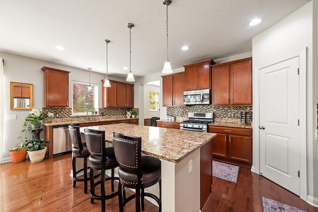 kitchen featuring a center island, stainless steel appliances, light stone counters, pendant lighting, and a breakfast bar area