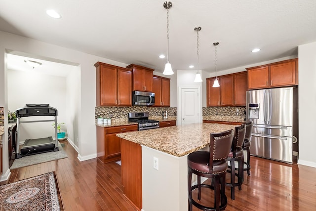 kitchen featuring a center island, a kitchen breakfast bar, hanging light fixtures, light stone countertops, and stainless steel appliances