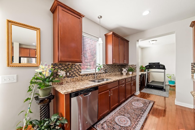 kitchen featuring light wood-type flooring, light stone counters, stainless steel dishwasher, sink, and decorative light fixtures